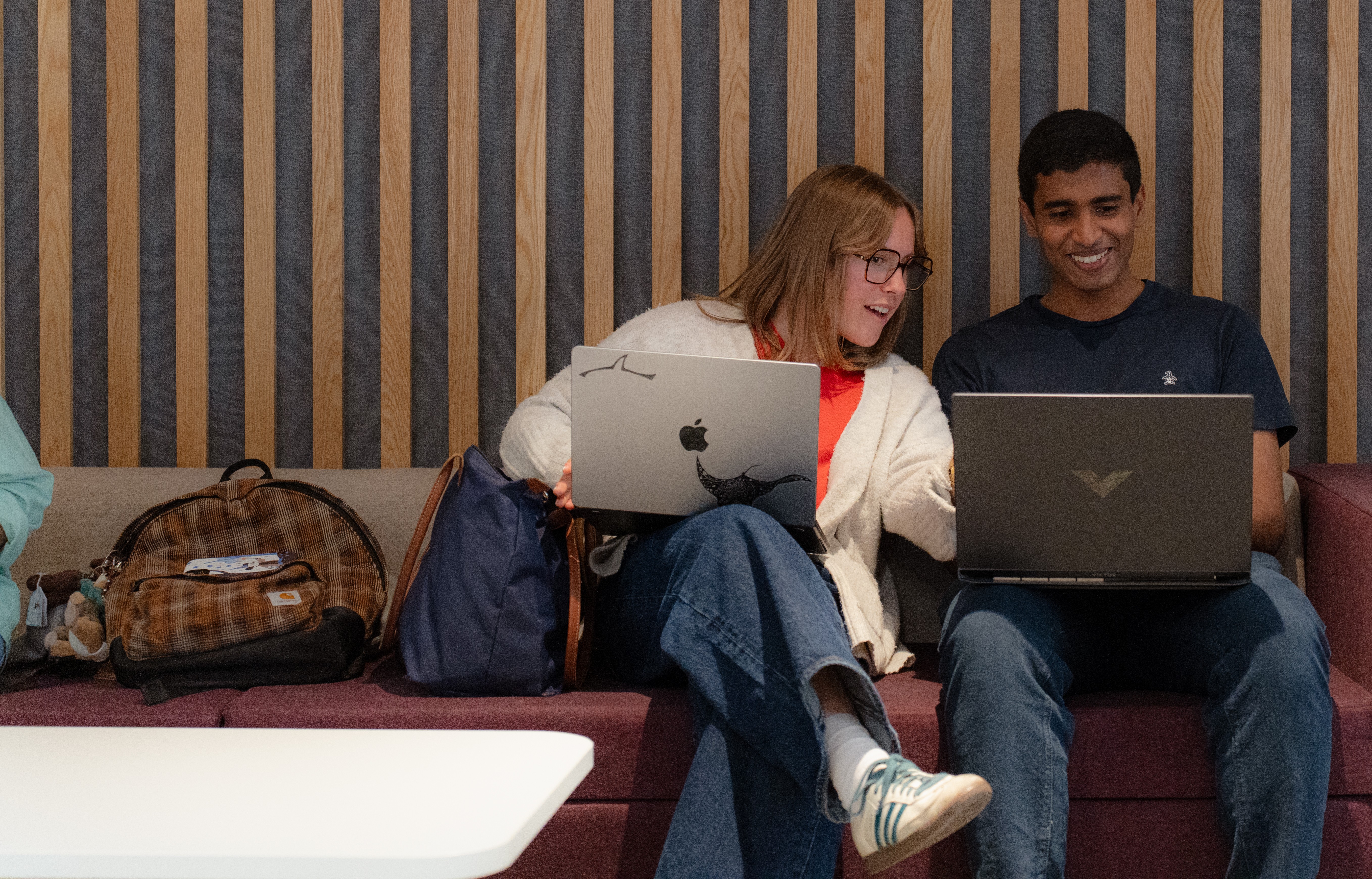 Two students sitting next to each other and looking at their laptop screens.